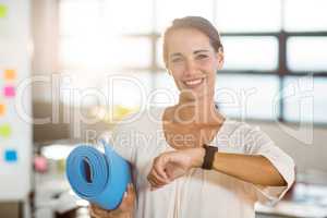 Portrait of female business executive holding exercise mat