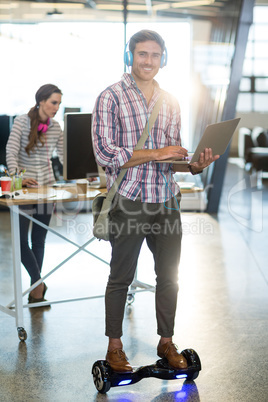 Smiling man standing on hoverboard and using laptop in office