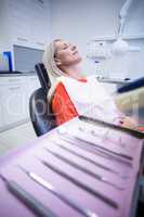 Woman relaxing on dentist chair with dental tools on foreground