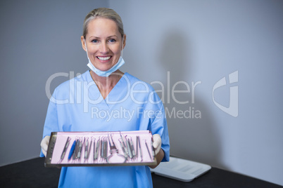 Smiling dental assistant holding tray with equipment in dental c