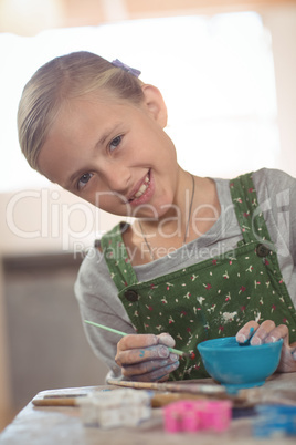 Smiling girl painting on bowl in pottery workshop