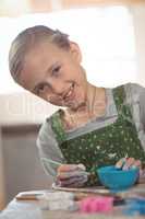 Smiling girl painting on bowl in pottery workshop