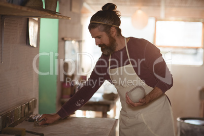 Male potter holding clay and cleaning table