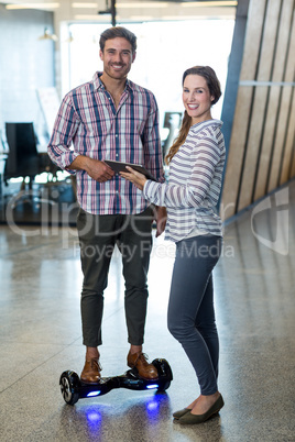 Man on hoverboard using digital tablet with colleagues in office