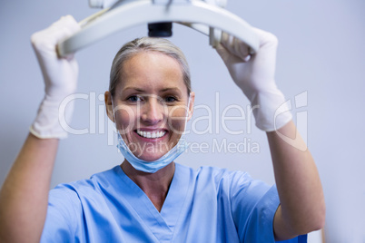 Smiling dental assistant adjusting light in clinic