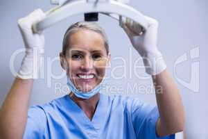 Smiling dental assistant adjusting light in clinic