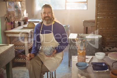 Smiling male potter painting on bowl