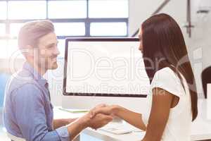 Businesswoman shaking hands with coworker while working on compu