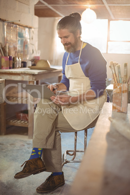 Male potter sitting on stool using laptop