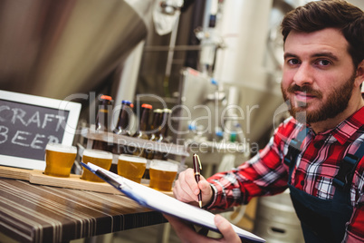 Manufacturer writing while examining beer in brewery