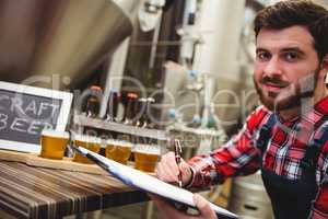 Manufacturer writing while examining beer in brewery