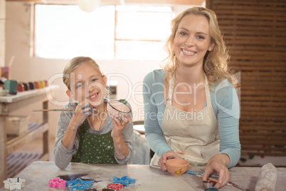 Smiling female potter and girl painting in pottery workshop