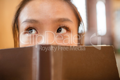 Thoughtful young woman cover her face with book