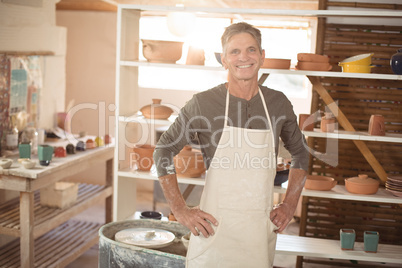 Smiling male potter standing with hand on hip in pottery worksho