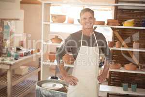 Smiling male potter standing with hand on hip in pottery worksho
