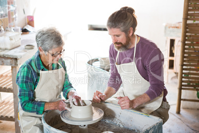 Male potter assisting female potter while making pot