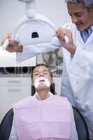 Smiling dentist adjusting light over patients mouth
