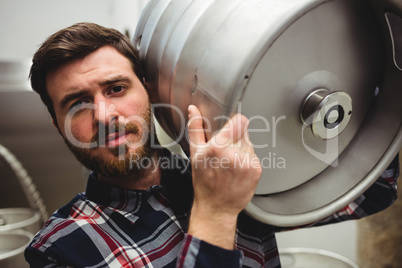Young manufacturer carrying keg in brewery
