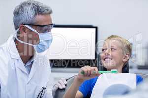Dentist assisting young patient while brush teeth