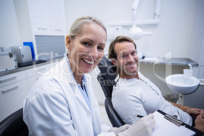 Female dentist writing on clipboard while interacting with male