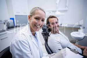 Female dentist writing on clipboard while interacting with male