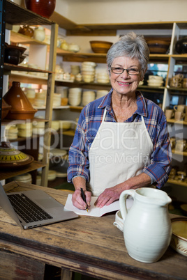 Portrait of female potter making note from laptop