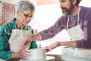 Male potter assisting female potter while making pot