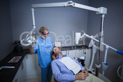 Smiling dentist assistant adjusting light over patients mouth