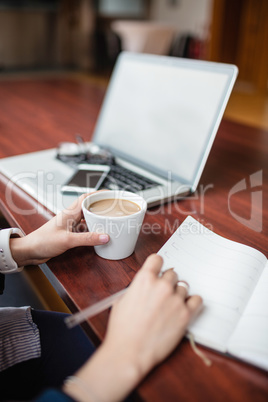 Woman writing in book while having tea