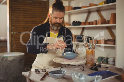 Attentive male potter painting on bowl