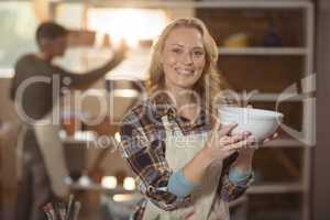 Smiling female potter checking bowl in pottery workshop
