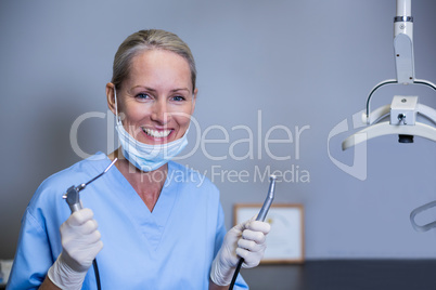 Smiling dental assistant holding dental tools in clinic