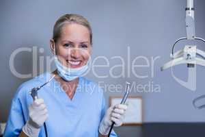 Smiling dental assistant holding dental tools in clinic