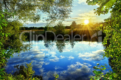 Sunrise over the river in the summer with reflection of clouds i