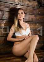 young beautiful naked woman sitting on the bench on a wooden wall background