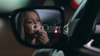 Young woman applying red lipstick in the car
