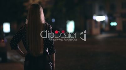 Charming girl hitchhiking on town street at night