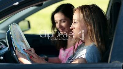 Two pretty girls in car paving travel route on map