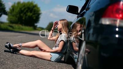Blonde girl sitting on road near her broken car