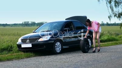 Young woman rolling spare wheel on road