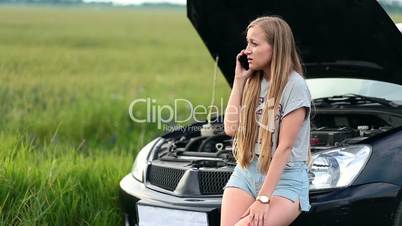 Upset woman talking on phone near broken car