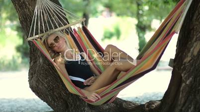 Woman lying in hammock in tree's shadow on beach