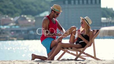 man applying sunscreen on girlfriends leg on beach