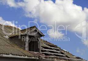 Old tile roof with holes and blue sky with clouds