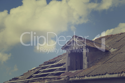 Old tile roof with holes and sky with clouds