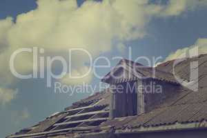 Old tile roof with holes and sky with clouds