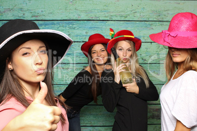 4 Mädchen mit Damenhüten und Sekt vor einer Fotobox - Mädchen zeigen Daumen hoch