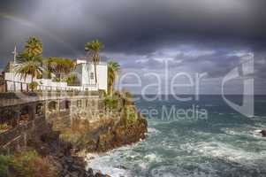 Town city hall over rocks and sea waves under a rainbow