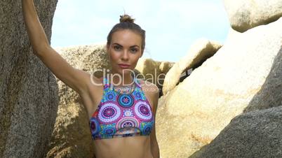 Pretty blonde woman between rocks near the sea during beautiful summer day