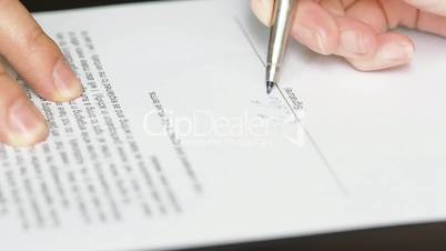 Closeup of businessman showing his new business partner where to sign an agreement or contract with fountain pen on rustic wooden desk.